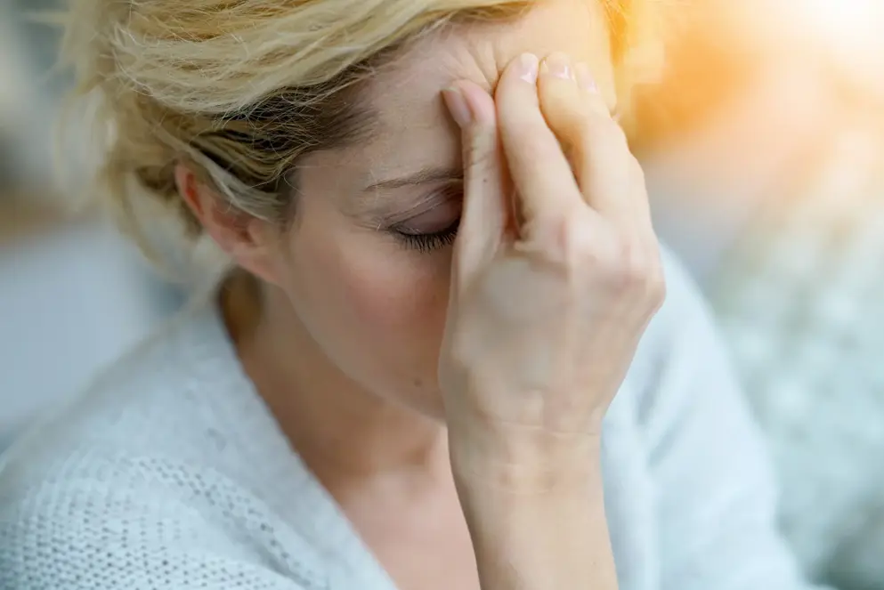 Woman holding forehead, eyes closed, suggesting headache or migraine discomfort. 