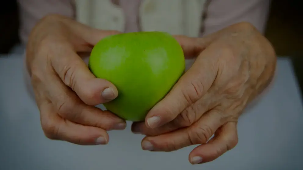 Close up of arthritic hands holding a green apple