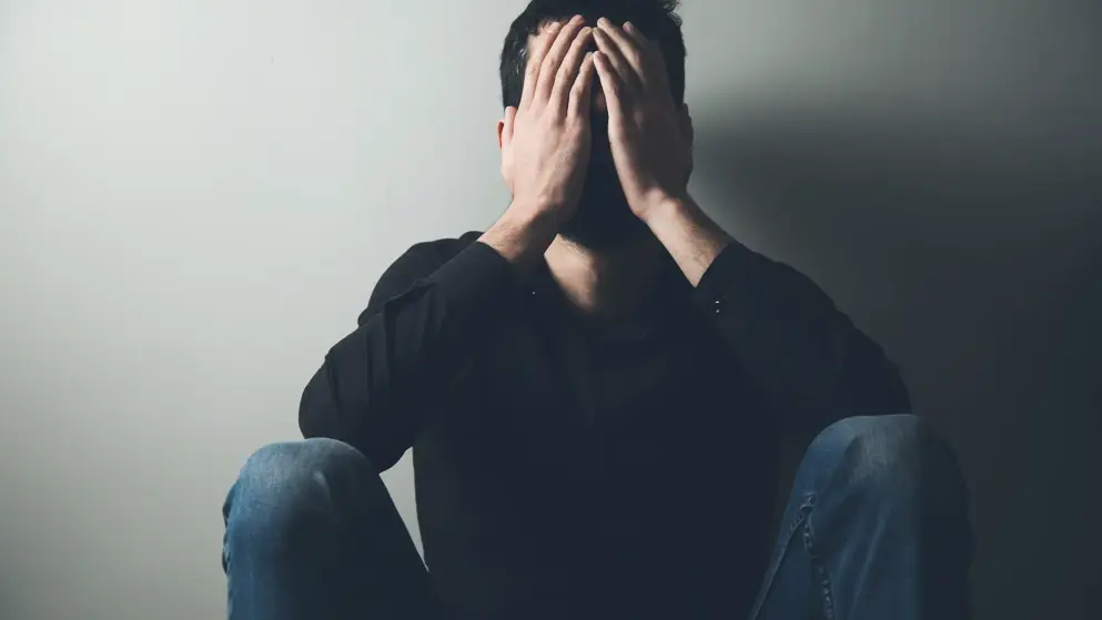 Young man sitting in the dark with his head in his hands