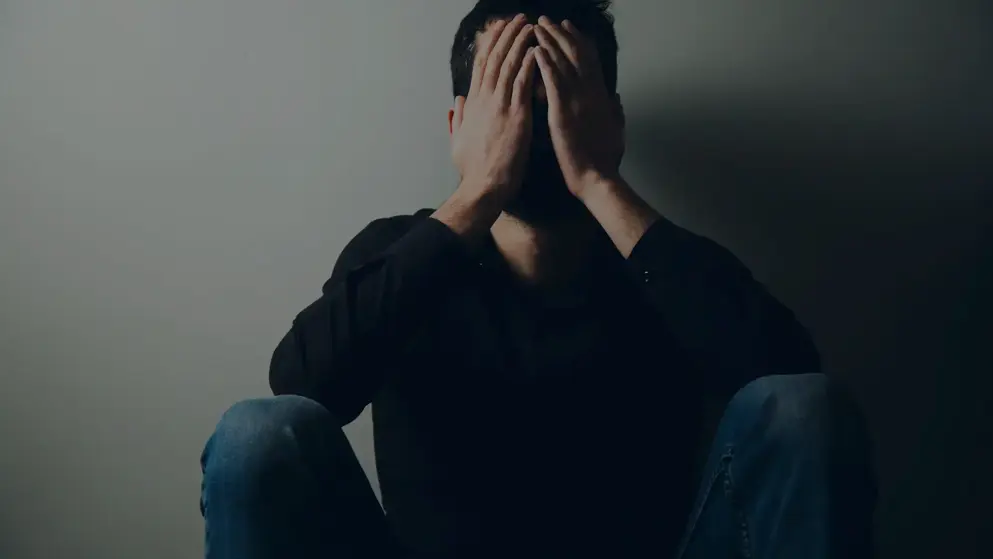 Young man sitting in the dark with his head in his hands