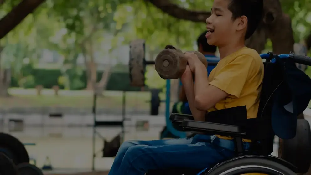 Young boy in a wheelchair with muscle wasting smiles while lifting a small hand weight